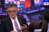 画面突然切回，BBC主播被拍到双脚翘桌看手机